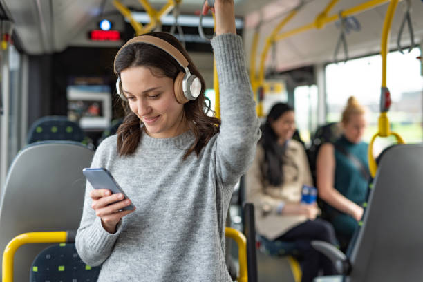 donna che usa il telefono cellulare e le cuffie mentre ascolta una musica in un autobus - bus transportation indoors people foto e immagini stock