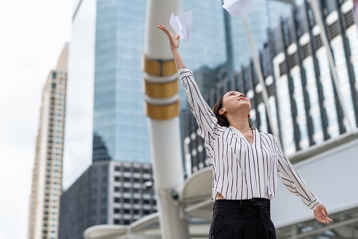 Portrait photo of a young asian beautiful businesswoman lady  throw away a pile stack of document paper in a central business district in Bangkok