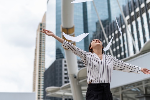 Portrait photo of a young asian beautiful businesswoman lady  throw away a pile stack of document paper in a central business district in Bangkok