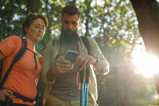 Selective focus shot of young man and his mature mother looking at GPS map coordinates on smart phone while on a hike in a forest.