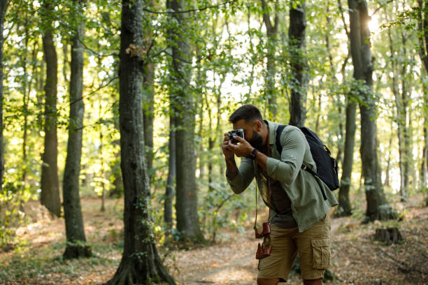 istock Young man using analog camera and taking photos of the trees during a forest hike 1426514262