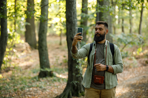 Copy space shot of young hipster backpacker holding his smart phone up, looking for signal during a forest hike.