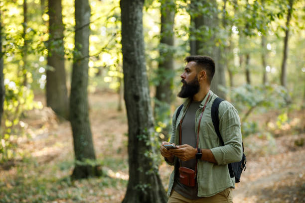 Copy space shot of young hipster backpacker standing on a trail in the forest, looking around, feeling lost during his hike.