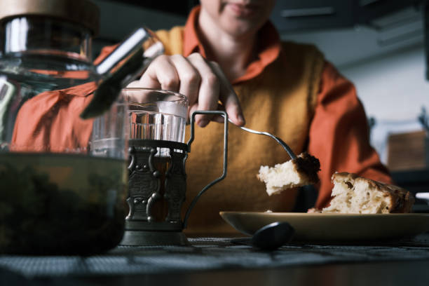 Woman is sitting in her kitchen, drinking hot tea, eating homemade plum cake and using smart phone