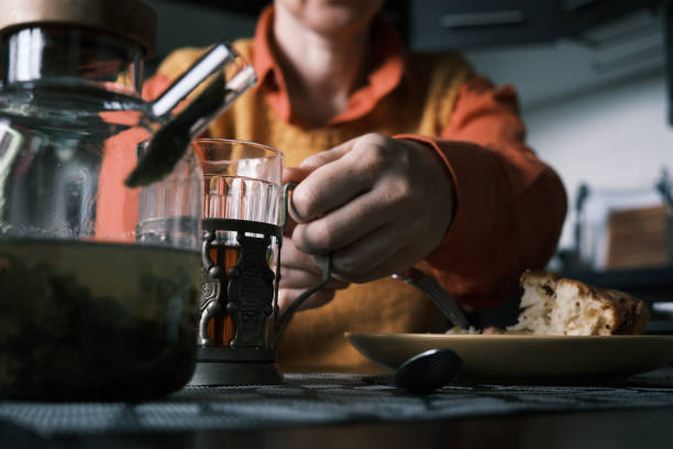 Woman is sitting in her kitchen, drinking hot tea, eating homemade plum cake and using smart phone