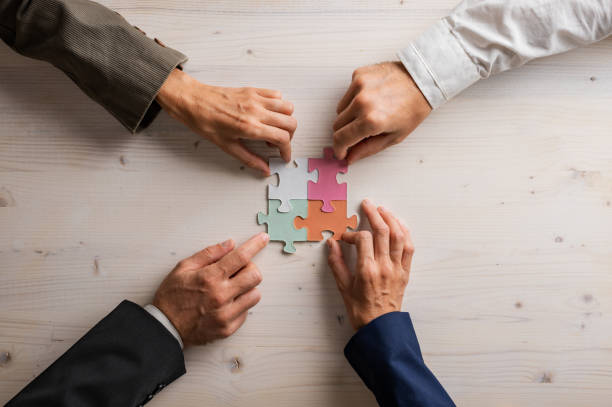 Hands of four businesspeople joining matching puzzle pieces stock photo