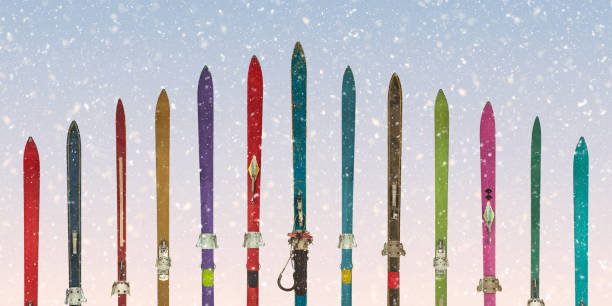 Row of vintage weathered skis in front of a blue sky with snowfall