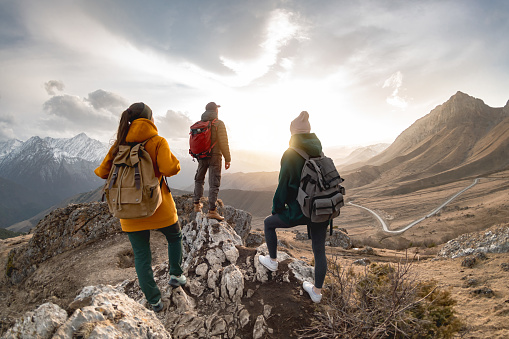 Group of hikers or tourists with backpacks walks in mountains at sunset