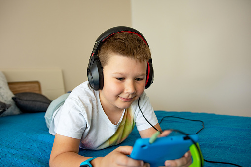 Portrait of happy boy in bed playing games on a tablet computer and smiling