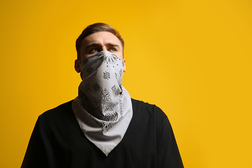 Young man with bandana covering his face on yellow background, low angle view