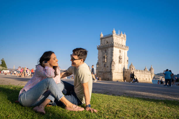 пара сидит на траве пер�ед торре-де-белен в лиссабоне - portuguese culture women ethnic smiling стоковые фото и изображения