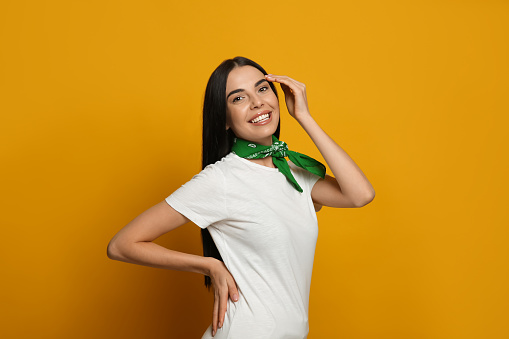 Young woman wearing stylish bandana on orange background