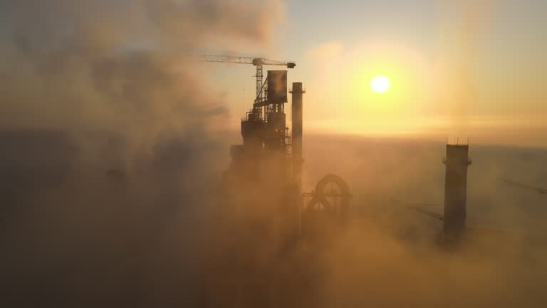 Aerial view of cement factory with high concrete plant structure and tower crane at industrial production site on foggy morning. Manufacture and global industry concept