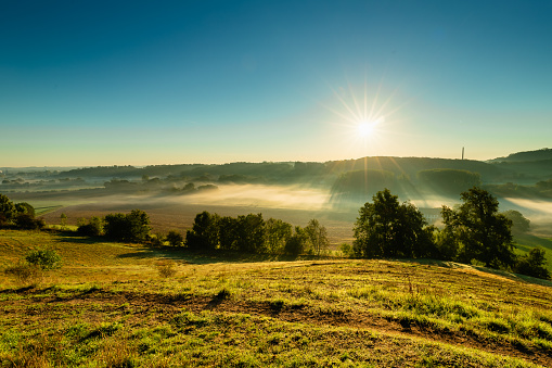 A view over the Jeker valley in the rolling hill landscape outside Maastricht, where the valley is covered with layers of fog and creating a nice setting with the sun beams through the mist over the fields