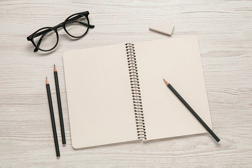 Flat lay composition with blank sketchbook on white wooden table. Space for text