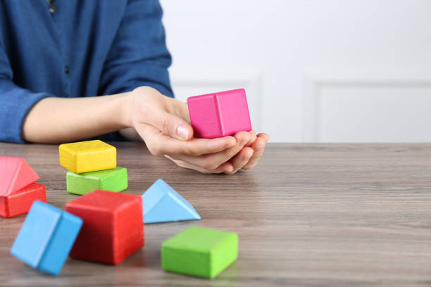 ABA therapist with colorful building blocks at wooden table, closeup