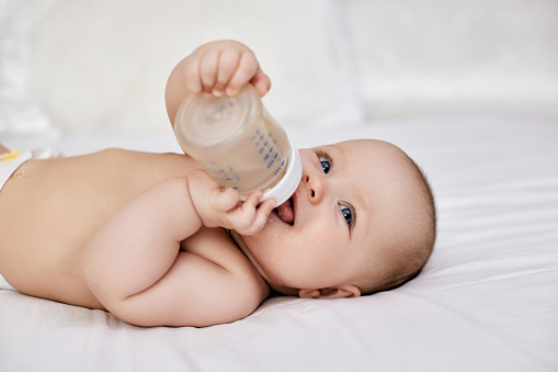 Charming baby girl lies in bed and drinks water from a bottle