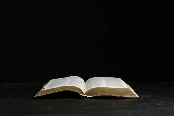 istock Open Bible on black table against dark background. Christian religious book 1426548512