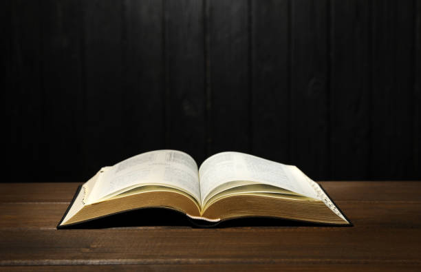 istock Open Bible on table against black wooden background. Christian religious book 1426548553