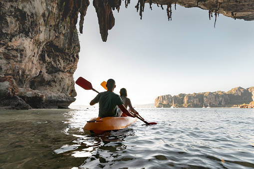 Young couple walks on kayak at tropical sea bay between cliffs. Kayaking or canoeing concept