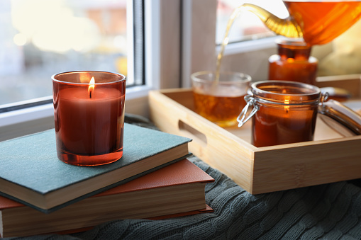 Burning candle on stack of books near window indoors