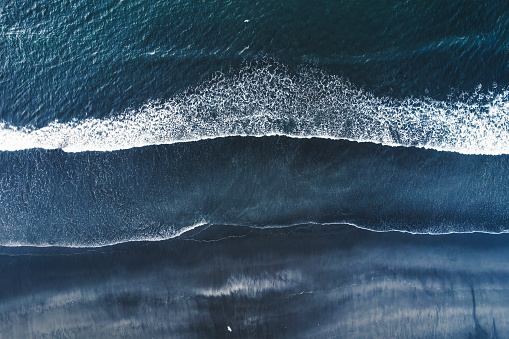 Aerial drone view of moody atlantic ocean wave on black sand beach in summer at Iceland
