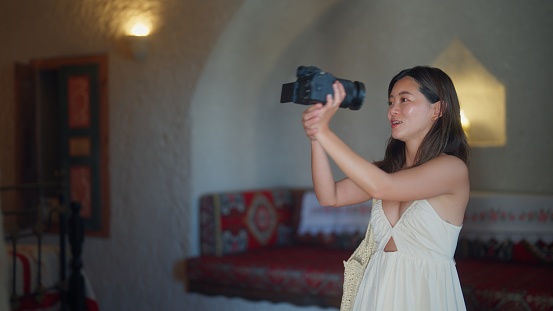 A female tourist vlogger, social media influencer is using her camera to vlog and introduce a hotel room in which she is going to stay during her vacation in a hotel.