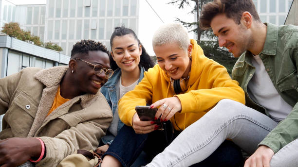 istock Group of smiling diverse young friends looking at mobile having fun. Millennial students in the park 1426552582