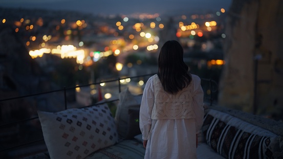 A female tourist is enjoying looking over the city from the rooftop of the hotel at night where she is staying during her travel.