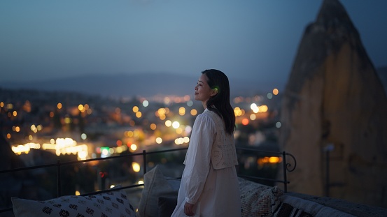 A female tourist is enjoying looking over the city from the rooftop of the hotel at night where she is staying during her travel.