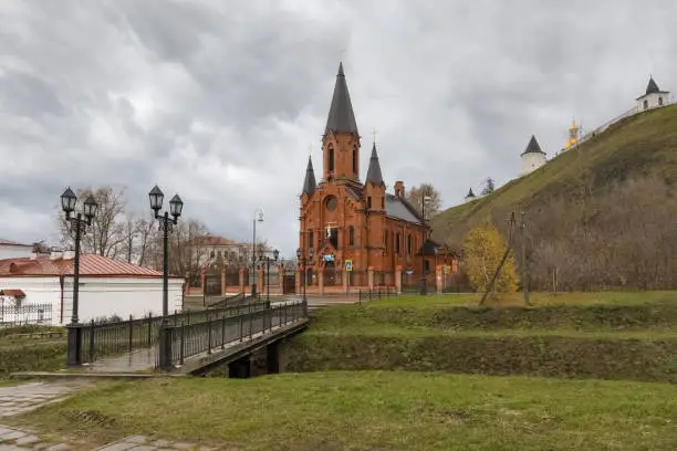 View of the majestic Catholic Cathedral and the Kremlin on a hill in Tobolsk (Siberia, Russia). Cityscape on an autumn rainy day. The gray textured sky matches the weather. Red brick church