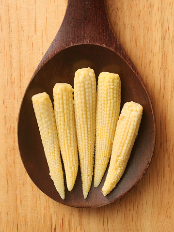 Top view of wooden spoon over table with baby corn on it