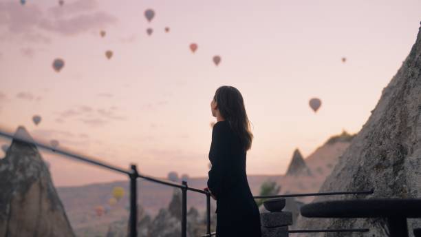 une touriste profite de regarder des montgolfières voler dans le ciel sur le toit de l’hôtel où elle séjourne pendant ses vacances - air travel photos et images de collection