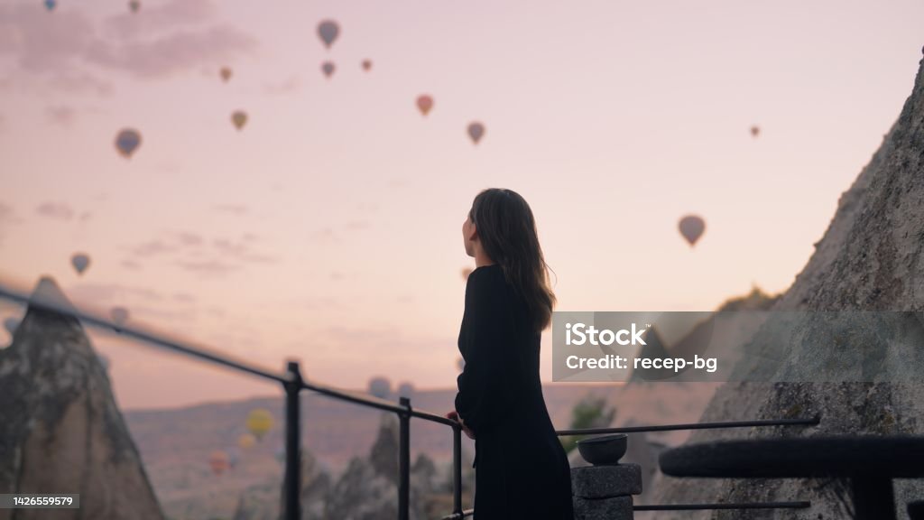 Female tourist enjoying watching hot air balloons flying in the sky at rooftop of hotel where she is staying during her vacation A female tourist is enjoying watching hot air balloons flying in the sky at the rooftop of the hotel where she is staying during her vacation. Day Dreaming Stock Photo