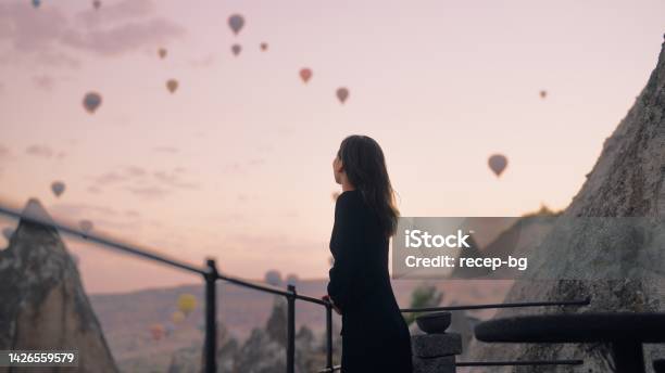 Female Tourist Enjoying Watching Hot Air Balloons Flying In The Sky At Rooftop Of Hotel Where She Is Staying During Her Vacation Stock Photo - Download Image Now