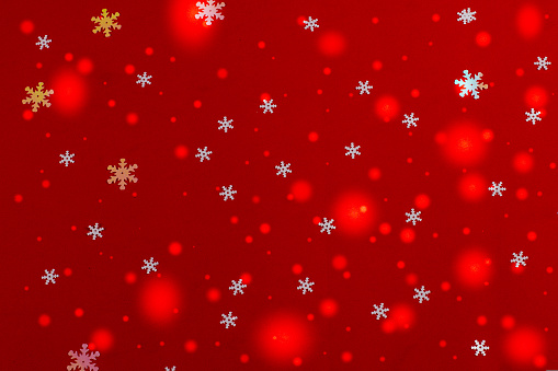 Falling white snowflakes and the glare of Christmas lights on a red background create a magical atmosphere of the Christmas holiday. Concept for festive wallpapers, backgrounds and postcards..