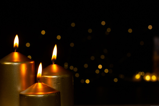 Golden wax candles burn evenly on Christmas night against the backdrop of garland lights. Relaxed family atmosphere. Concept of christmas and new year..