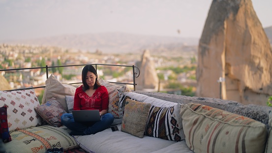 A young female freelancer tourist is using her laptop at the rooftop patio of the hotel where she is staying during her travel.