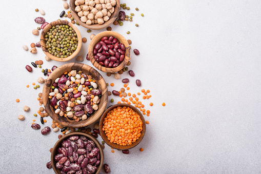 Top view of different beans, lentils, mung, chickpeas in wooden bowls for tasty meals on grey concrete background