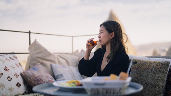 A female tourist is enjoying having breakfast on the rooftop of the hotel where she is staying during her travel.