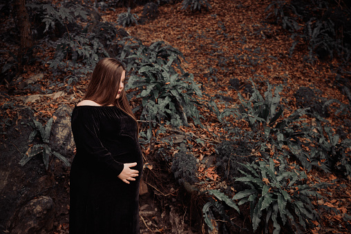 Beautiful and long-haired pregnant woman portrait with eyes closed wearing black dress