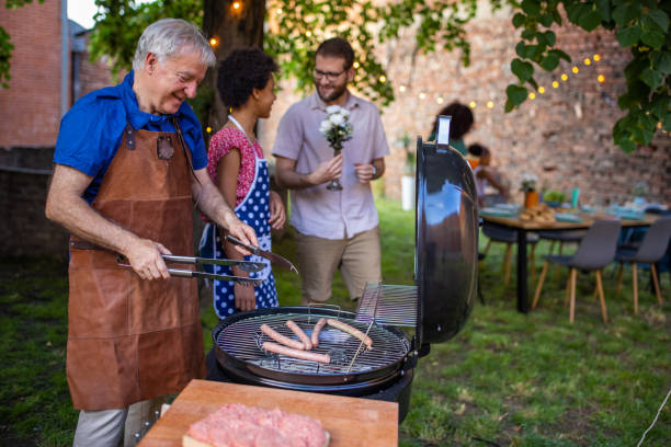 istock Senior man grilling sausages at a back yard barbecue party 1426567979