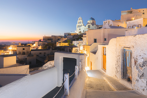 A narrow old town lane in the quaint village of Pyrgos Kallistis leads to the traditional blue dome Greek Orthodox Saint George Church on the island of Santorini, Greece at blue hour.