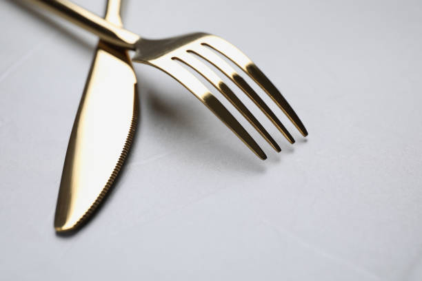 istock Golden fork and knife on light grey table, closeup. Space for text 1426574084