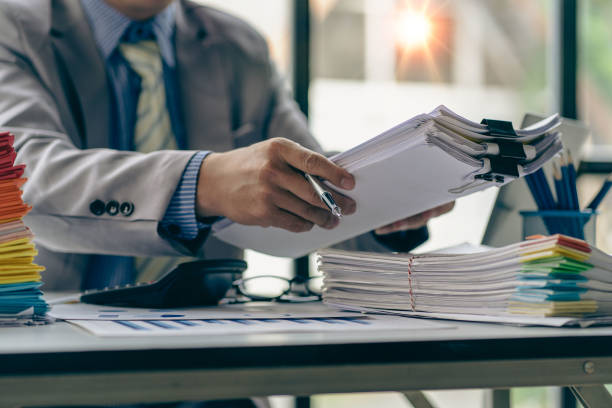 Businessman working in finance with pile of unfinished papers on the desk business paper pile stock photo