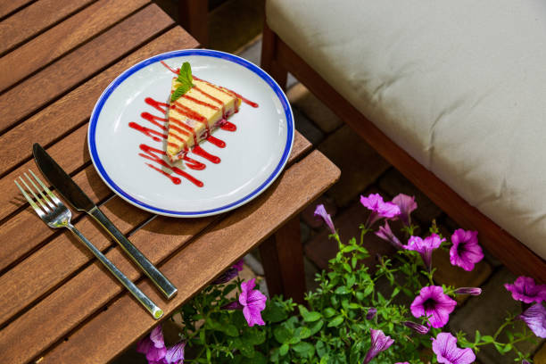 Cheesecake with jam and mint in a plate on the bedside table with cutlery against a background of flowers