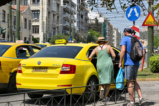 Athens, Greece - May 2022: Two people getting in a yellow taxi on one of the city streets