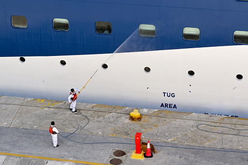 Corfu, Greece - June 2022: Crew from a Marella cruise ship using a high powered jet washing equipment to clean the side of the vessel