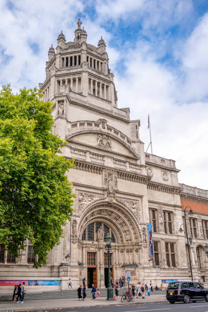 People outside the elaborately carved Grand Entrance to the Victoria and Albert Museum (1857 onwards), South Kensington, London, England. Statues of Prince Albert and of Queen Victoria