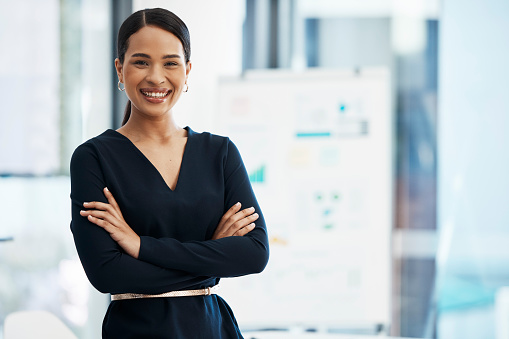 Confident, happy and smiling business woman standing with her arms crossed while in an office with a positive mindset and good leadership. Portrait of an entrepreneur feeling motivated and proud